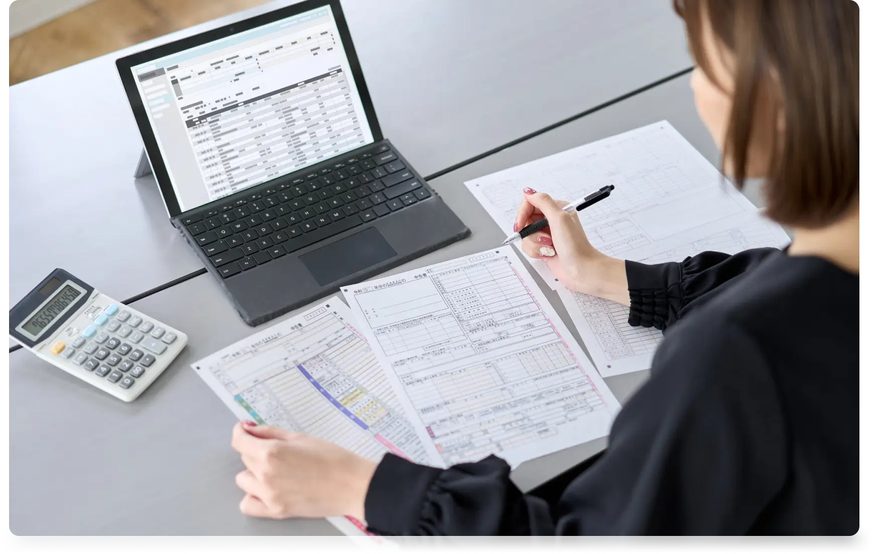 Woman working on paperwork with laptop.
